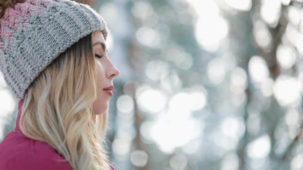 Mujer bonita en sombrero de invierno disfruta de la nieve de pie fuera en la nieve en el bosque. Ella sonrió, respirando hondo. Vídeo en cámara lenta — Vídeo de stock