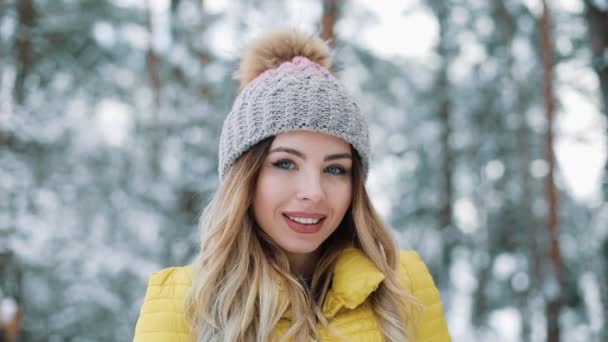 冬天的画像一个迷人的年轻女子看着相机微笑的女孩在黄色羽绒服站在冬季森林. — 图库视频影像