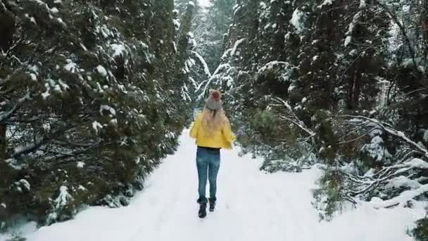 Jente i gul jakke løper rundt i en vinterskog dekket av snø – stockvideo