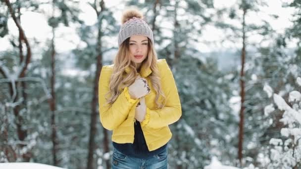 Portret zimowy uroczy młoda kobieta, patrząc na kamery dziewczyny Smiling w żółty Kurtka puchowa stoi w lesie zimą — Wideo stockowe