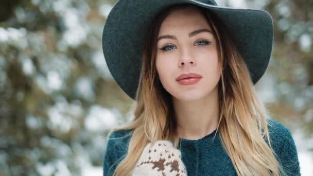 Retrato de la mujer hermosa joven con estilo en abrigo verde y sombrero pasea por el bosque de invierno. En cámara lenta. La joven Bautiful camina en invierno — Vídeos de Stock