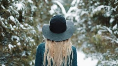 Arkadan Bayan yeşil şapka ve bir kış orman yürüyüş bir kat bak. Kız görünüyor ve kameraya poz veriyor