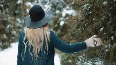Yeşil şapkanı ve paltonu baştan çıkarıcı kadın kış orman yürür ve ağaçlar dokunur. Kız görünüyor ve kameraya poz veriyor