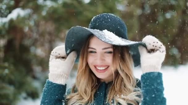 Senhora de chapéu verde e casaco fica sob a neve caindo na floresta — Vídeo de Stock