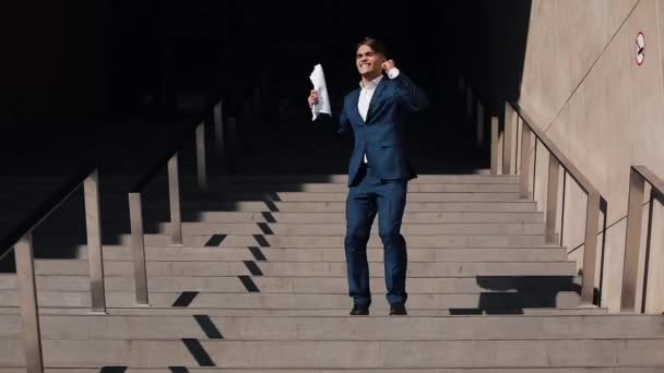 The young successful businessman leaves the office building with a signed contract. He is happy and funny dancing on the street. Slow motion. Business, paperwork, vacation, contract, lifestyle — Stock Video