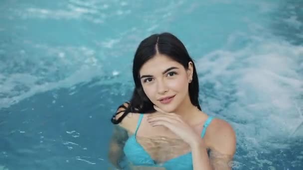 プールで競泳水着立っている美しい少女は、動きを遅きます。クローズ アップ。カメラにポーズ プールでセクシーな官能的なウェットの女の子の肖像画 — ストック動画