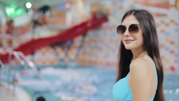 Σέξι γυναίκες στο μπλε μαγιό και γυαλιά ηλίου που θέτουν σε πισίνα. Πορτρέτο του ένα ελκυστικό κορίτσι σε ένα υδάτινο πάρκο, εξετάζοντας τη φωτογραφική μηχανή — Αρχείο Βίντεο