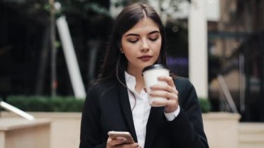 Profesyonel genç iş kadını Smartphone ve içecek kahve kullanarak kentsel sokakta yürümek. Konsept: yeni iş, iletişim, bankacı. Dış, ağır çekim