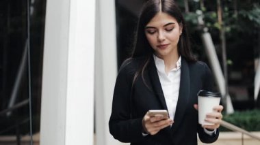 Profesyonel genç iş kadını Smartphone ve içecek kahve kullanarak kentsel sokakta yürümek. Konsept: yeni iş, iletişim, bankacı. Dış, ağır çekim