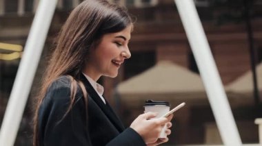 Profesyonel genç iş kadını Smartphone ve içecek kahve kullanarak kentsel sokakta yürümek. Konsept: yeni iş, iletişim, bankacı. Dış, ağır çekim