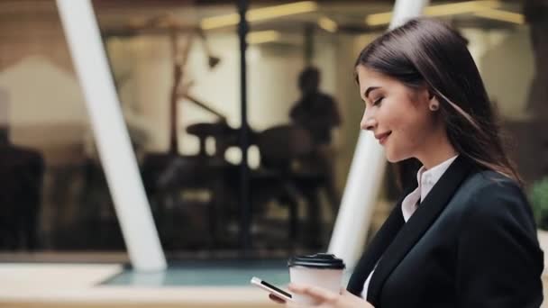 Joven empresaria profesional que camina por la calle urbana con un smartphone y bebe café. Concepto: nuevo negocio, comunicación, banquero. Afuera, cámara lenta — Vídeos de Stock