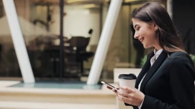 Profesyonel genç iş kadını Smartphone ve içecek kahve kullanarak kentsel sokakta yürümek. Konsept: yeni iş, iletişim, bankacı. Dış, ağır çekim