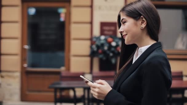 Jovem mulher de negócios bonita usando smartphone e andando na rua velha. Ela está a navegar na Internet. Conceito: novo negócio, comunicação, banqueiro, gerente — Vídeo de Stock