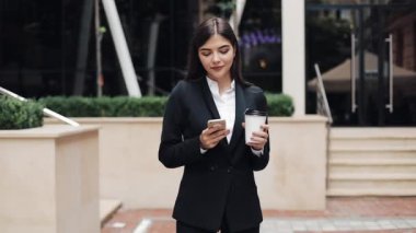 Profesyonel genç iş kadını Smartphone ve içecek kahve kullanarak kentsel sokakta duruyor. O kamera kavramı arıyorum: yeni iş, iletişim, bankacı. Dış, ağır çekim