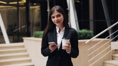 Profesyonel genç iş kadını Smartphone ve içecek kahve kullanarak kentsel sokakta duruyor. O kamera kavramı arıyorum: yeni iş, iletişim, bankacı. Dış, ağır çekim