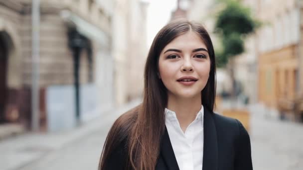 Jonge mooie zakenvrouw of student in pak lopen in de straat. Ze glimlachen, gelukkig en kijken in de camera. Concept: nieuwe business, communicatie, bankier, manager — Stockvideo