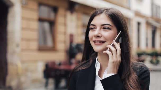 Linda jovem mulher de negócios feliz falando em seu telefone, andando, ri. Estilo de vida de negócios, estilo de vida ativo, mulher moderna. Humor alegre — Vídeo de Stock