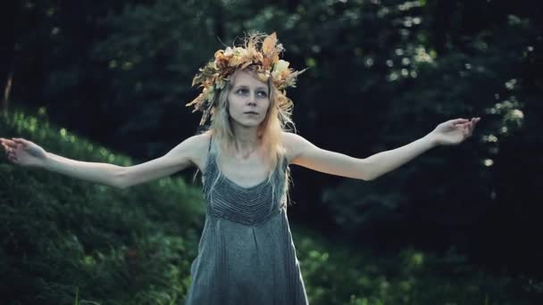 Мистическая девушка в лесу проводит ритуал. Она была одета в длинные платья с венком на голове. Ведьмы, эзотерические сеансы, магия, гадание, потусторонние силы — стоковое видео