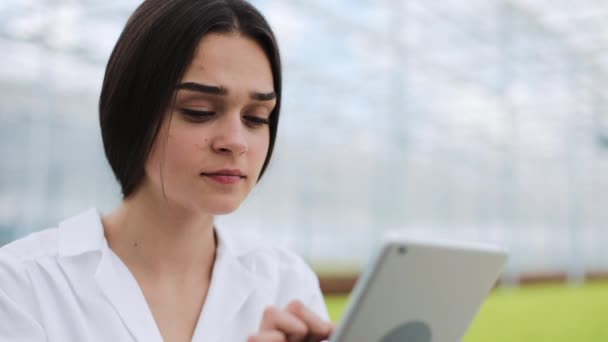 Ingénieur agricole en serre vêtu d'un manteau blanc travaillant sur tablette pour tester la santé des pantalons et analyser les données avec tablette — Video