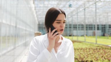 Çalışan mobil ve konuşmak smartphone kullanarak bir sera yürüyüş. Serada çalışan ziraat mühendisi