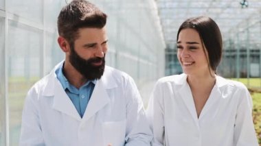 İki araştırmacı laboratuvar cüppeli sera yürümek. Onlar iş yapma başarısını tartışmak
