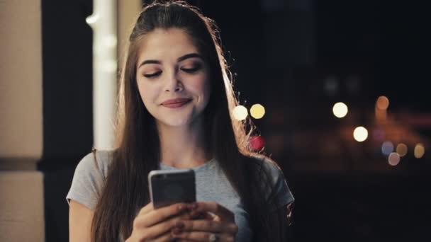 Ελκυστική νεαρή γυναίκα χρησιμοποιώντας smartphone στέκεται στον δρόμο της νύχτας πόλη ευτυχώς αντιδρούν στο μήνυμα. Σύγχρονες τεχνολογίες, επιτυχημένη — Αρχείο Βίντεο