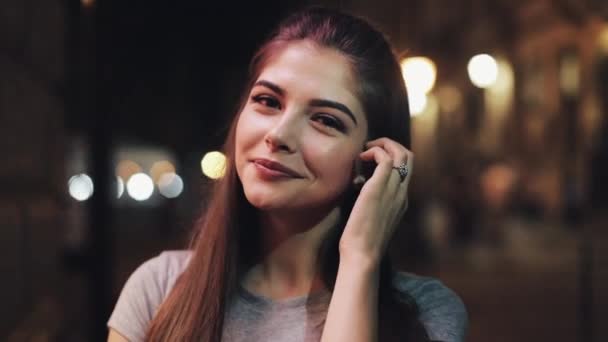 Retrato de uma jovem mulher atraente na rua da cidade noturna. Happy Girl a olhar para a câmara. Noite turva — Vídeo de Stock