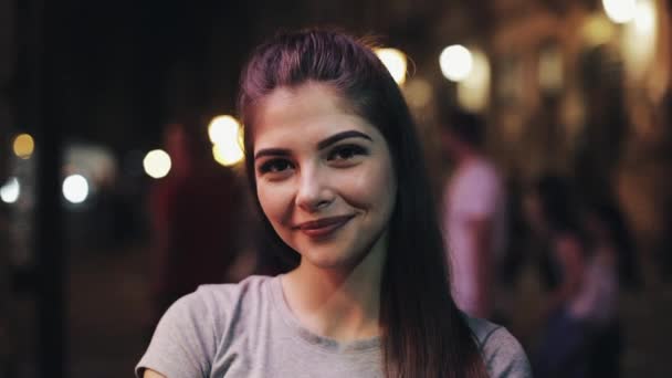 Retrato de uma jovem mulher atraente na rua da cidade noturna. Happy Girl a olhar para a câmara. Noite turva — Vídeo de Stock