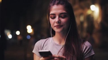 Çekici genç kadın müzik ve smartphone kullanarak kulaklarını kulaklıklarla. Bulanık gece