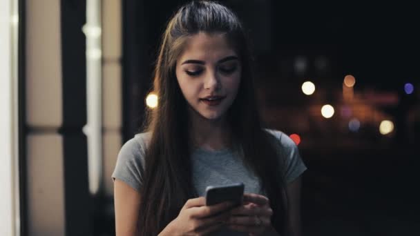 Attraktiv ung kvinna ringer upp ett telefonnummer och samtalen om den smartphone som går på gatan av natt stad. Vackra mångkulturella ung avslappnad kvinnlig professionell på mobiltelefon — Stockvideo