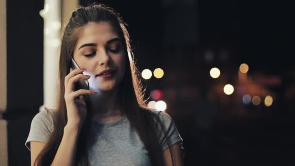 Молодая красивая женщина разговаривает по смартфону ночью на освещенной улице. Смартфон, концепция технологии — стоковое видео