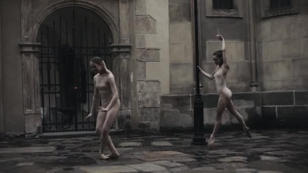 Молодые профессиональные танцовщицы исполняют акробатический танец по средневековой улице под дождем. Мокрые девушки танцуют в каплях воды, замедленная съемка — стоковое видео