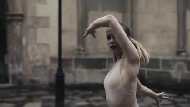 Young professional female dancers is performing acrobatic dance along the medieval street under the rain. Wet girls dancing in water drops, slow motion — Stock Video