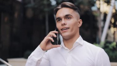 Sokak ofisinde görüştükten sonra veya iş günü sonra yürüme ve bir gülümseme ile telefonda konuşan genç başarılı iş adamı. Dışarıda