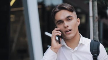 Mutlu ypung işadamı telefonu konuşurken bir sırt çantası ile. Modern Ofis Binası yakınındaki ayakta. Konsept: teknoloji, telefon, iş gezileri, iş