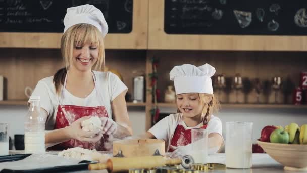 Mom and daughter in the same clothes have fun preparing a dough on a cozy kitchen. They preparing Christmas cookies. Family day, Cooking, Mom and daughter concept — Stock Video