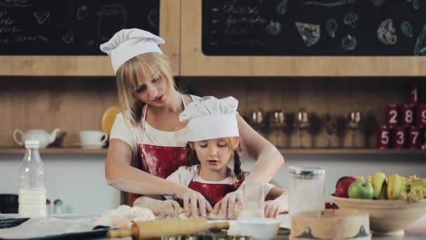 Mamá e hija con la misma ropa se divierten preparando una masa en una cocina acogedora. Están preparando galletas de Navidad. Día de la familia, Cocina, Concepto de mamá e hija — Vídeos de Stock