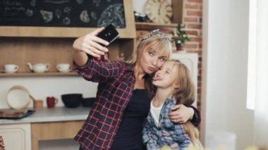 Gülümseyen anne ve kızı evde mutfak smartphone kamera ile selfie fotoğraf yapma. Aile, aşçı ve insanlar kavramı