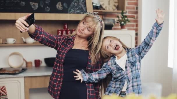 Sonriente mamá y su hija haciendo foto selfie con cámara de teléfono inteligente en casa en la cocina. Concepto de familia, cocinero y gente — Vídeos de Stock