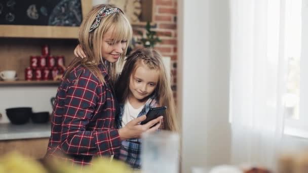 Glada mor och dotter bläddrar smartphone tillsammans och ler på morgonen i köket hemma — Stockvideo