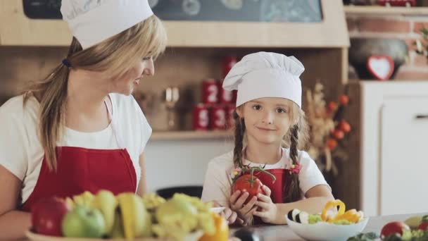 Mamá y su hijita cocinan en la cocina: hacen una ensalada de jardín fresco, y la madre enseña a la niña. — Vídeos de Stock
