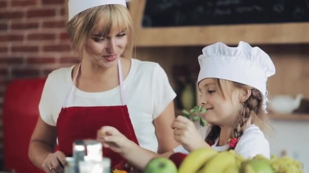 Mamá y su hijita cocinan en la cocina: hacen una ensalada de jardín fresco, y la madre enseña a la niña. — Vídeos de Stock