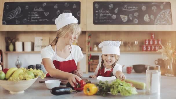 妈妈和小女儿在厨房做饭: 他们做一个新鲜的花园沙拉, 妈妈教女孩。烹饪和幸福的家庭概念 — 图库视频影像