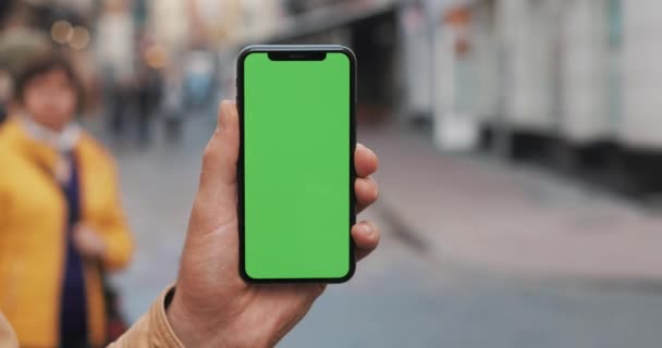 Tæt på skud af mand hænder holder smart telefon med grøn skærm på byens gadebaggrund. Chroma nøgle – Stock-video