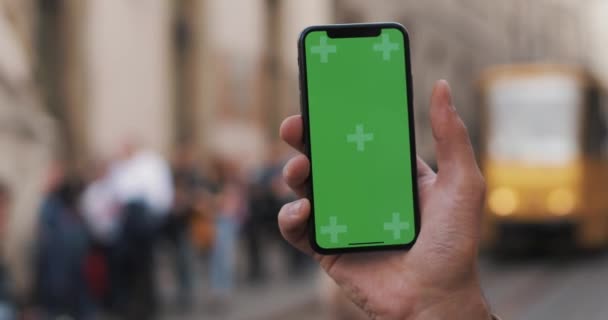 Primer plano de una mano de hombre sosteniendo un teléfono móvil con una pantalla verde vertical en las calles — Vídeos de Stock