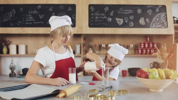 Mama i córka w kuchni przytulne. Małą córeczkę nalewa mleko do kieliszka. Pojęcie śniadanie, gotowanie — Wideo stockowe