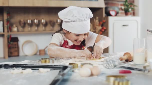 Schattig klein meisje maken van cookies van ruwe deeg in de vorm van bloemen en sterren. Dochtertje met moeder maakt cookies thuis in de keuken — Stockvideo