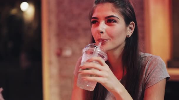 Jovem mulher bonita bebe um coquetel sentado em um bar ou restaurante perto de sinalização de néon — Vídeo de Stock