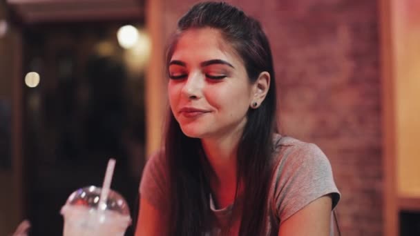 Bir bar veya restoran neon tabela yakınındaki bir kokteyl oturan genç güzel kadın içecekler — Stok video