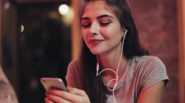 Müzik dinlerken gülümseyerek, bir kokteyl içme bir barda oturmuş, bir smartphone kullanarak güzel ve genç birbayan. O genç bir adamın yanına oturur